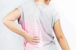 Foto di una donna con una maglietta grigia che si afferra la schiena dolorante