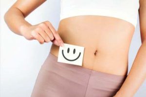 Photo de la région abdominale d'une femme tenant un post-it avec un smiley devant son ventre