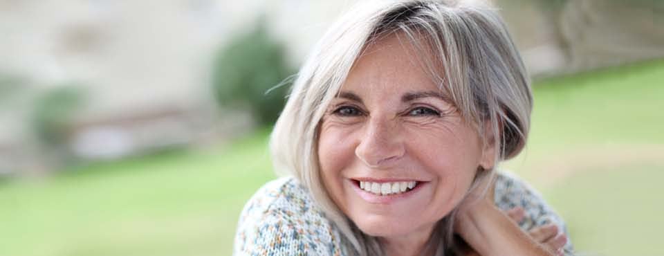 Frau in den 50zigern vor unscharfem lächelt den Betrachter zufrieden an