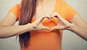 You can see the torso of a woman in orange t-shirt forming a heart with her hands over her heart