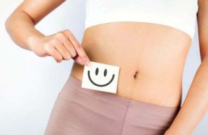 Close up of woman with belly top - in front of belly she holds note with laughing smiley face