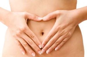 Close up of slim woman forming heart with hands on her belly around navel
