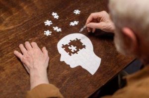 Aufnahme eines alten Mannes der versucht ein Puzzle in Form eines menschlichen Kopfes zu lösen