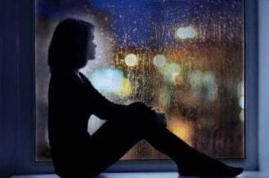 Ripresa di una donna seduta alla finestra, che osserva tristemente e pensierosa le strade piovose.
