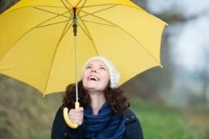 Scatto di una donna felice e in salute che sfida la pioggia autunnale con un ombrello giallo brillante.