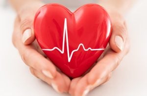 Due mani tengono protettivamente un cuore rosso con una linea di frequenza impressa.