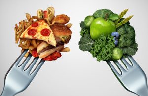 Two forks - on the left fork are poked unhealthy, fatty foods and on the right you can see healthy vegetables and fruits