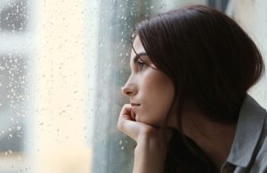 Close up of young woman looking at outside sitting at window with apathetic look