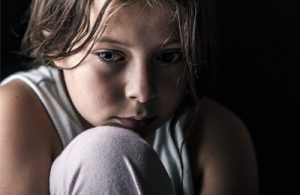 Fotografia de uma rapariga acovardada com um olhar triste numa sala escura