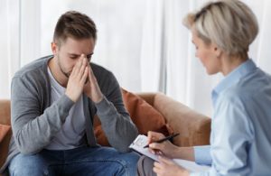 Therapist with takes notes while listening to male patient who appears depressed