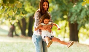 Une jeune femme dans un parc tient une petite fille heureuse dans ses bras et se tourne vers elle.