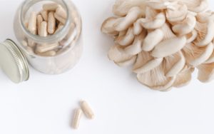 Image of a jar with mushroom powder capsules next to a fresh Pleurotus mushroom on white background.