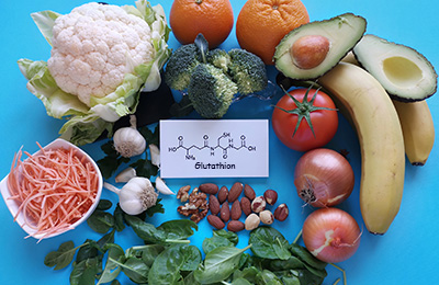 Gesundes Gemüse und Obst auf blauem Untergrund, dazwischen liegt ein weißer Zettel mit der chemischen Formel von Gluthathion
