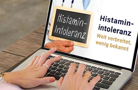Frauenhände auf der Tastatur eines Laptops - auf dem Bildschirm ist eine Fachinformation zum Thema Histaminintoleranz zu sehen