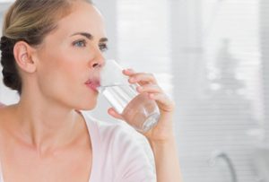 Aufnahme einer Frau, die ein Glas Wasser trinkt - softer , unscharfer Hintergrund mit Jalousien