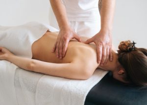 Gravação de uma situação de massagem. Uma mulher está deitada de bruços sobre um banco de massagem e está a ser medicamente massajada por um homem.