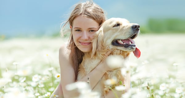 Junge Frau sitzt in der Natur mit ihrem Hund, umgeben von einem Feld von Magariten